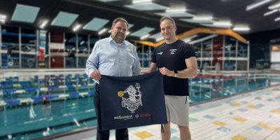Zwei Männer stehen in einem Schwimmbad und halten ein Banner mit dem Logo des Wasserballvereins Poseidon Koblenz, Bosch und Weisgerber.