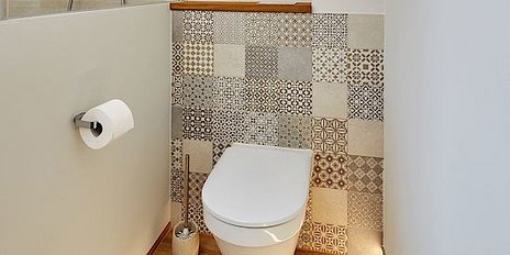 Eine saubere Toilette steht vor einer dekorativen Wand mit verschiedenen Fliesenmustern und einem Handtuchhalter.