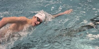 Ein junger Schwimmer mit einer weißen Badekappe und Schwimmbrille schwimmt kraftvoll durch das klare Wasser eines Schwimmbeckens.