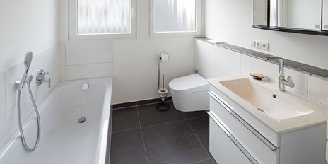 Ein gut beleuchtetes Badezimmer mit weißen Fliesen, einem modernen Waschbecken und einem komfortablen WC in einem schlichten Design.