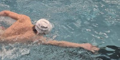 Ein Schwimmer führt einen kraftvollen Armzug im Wasser aus, während Spritzer um ihn herum aufsteigen.