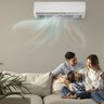 Im Wohnzimmer sitzt eine Frau mit Tochter auf dem Sofa und der Mann steht hinter den beiden. Alle schauen sich glücklich an. An der Wand im Hintergrund ist eine Klimaanlage, die Frische Luft in den Raum bringt.