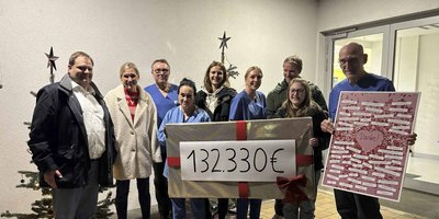 Eine Gruppe von Menschen steht vor einem Gebäude, hält ein großes Schild mit der Summe von 132.330 € und zeigt Dankbarkeit.