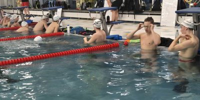 Eine Gruppe von Schwimmern in einem Hallenbad, die sich auf das Training vorbereiten und ihre Schwimmbrillen anpassen.