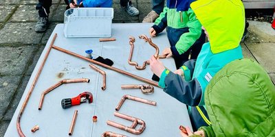 Eine Gruppe von Kindern arbeitet an einem Tisch mit Kupferrohren und Werkzeugen, während sie kreativ basteln.