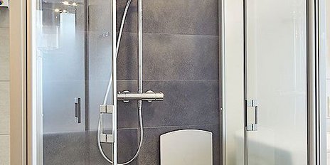 Eine moderne Dusche mit gläsernen Wänden, einem Regenduschkopf und einem klappbaren Sitz auf der linken Seite.