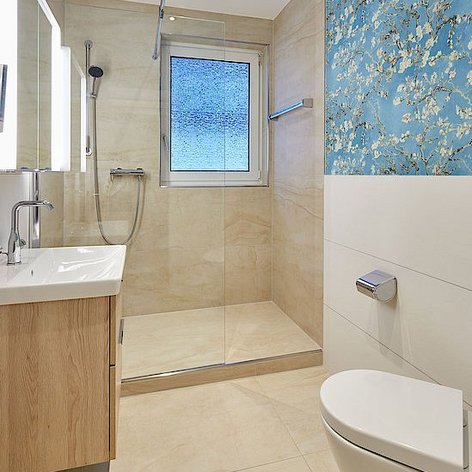 Ein modernes Badezimmer mit einer gläsernen Dusche, einem Holzwaschtisch und einer blauen Wand mit floralen Mustern.