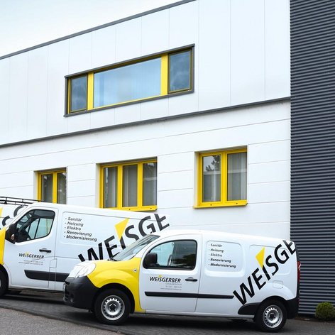 Drei Lieferwagen mit dem Logo 'WEISGERBER' stehen vor einem modernen, hellen Gebäude mit gelben Fenstern.