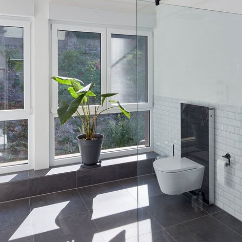 Ein modernes Badezimmer mit großen Fenstern, einer Pflanze in einem Topf und eleganten, weißen Fliesen an den Wänden.