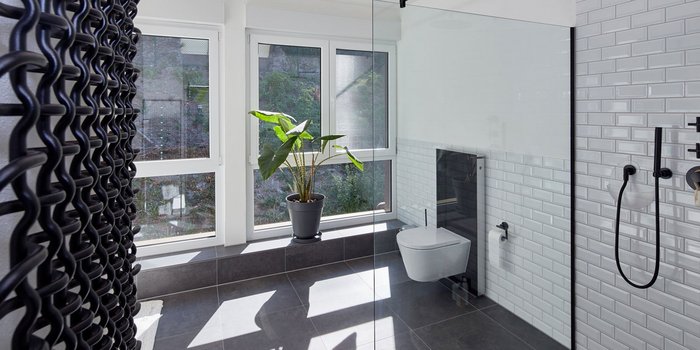 Ein modernes Badezimmer mit großen Fenstern, einer Pflanze in einem Topf und eleganten, weißen Fliesen an den Wänden.