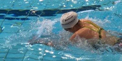 Eine Schwimmerin mit einem weißen Badekappe schwimmt kraftvoll durch das klare Wasser eines Schwimmbeckens.