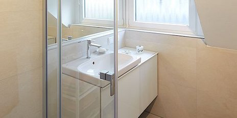 Ein modernes Badezimmer mit einer gläsernen Duschkabine und einem eleganten Waschbecken unter einem Fenster.